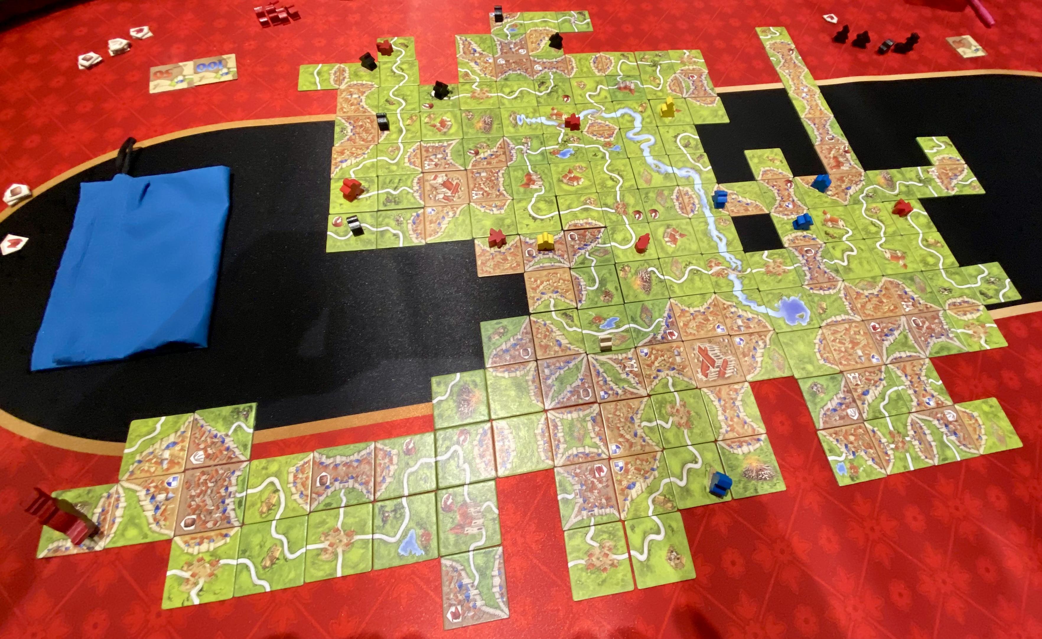 This is a game of Carcassonne, a tile-placement board game. Players build a medieval landscape with tiles featuring cities, roads, monasteries, and fields. They place followers, called meeples, to claim features and score points.